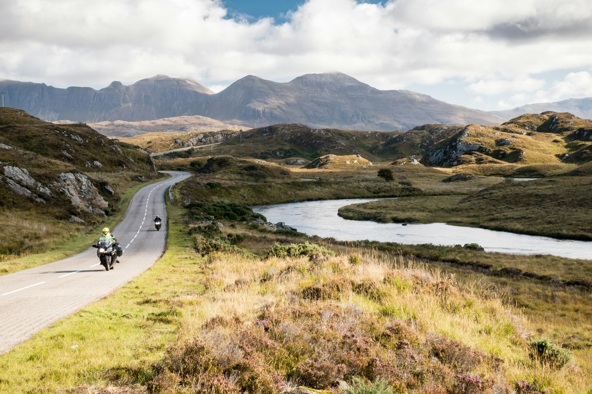 The A837 road, part of the North Coast 500 route, meanders past rivers and low hills in the glacial landscape of Assynt, with Quinag mountain in the distance, in the Northwest Highlands of Scotland 